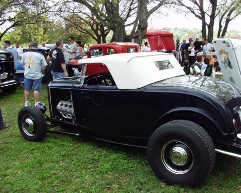 1996 Ford Bronco - A dark blue convertible hot rod with a white top is parked on the grass at an outdoor event.