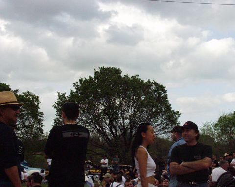 1996 Ford Bronco - An outdoor event with attendees mingling around various vehicles under a cloudy sky.