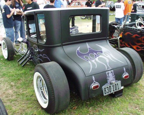 1996 Ford Bronco - Three-quarter rear view of a satin-black 1920s-era Ford Model T hot rod coupe at an outdoor car show, wearing white pinstriped flames and p…