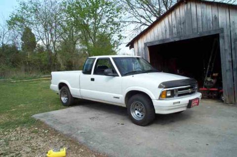 1988 Ford Bronco - This white Chevrolet S-10 pickup truck is parked outside a rustic wooden shed.