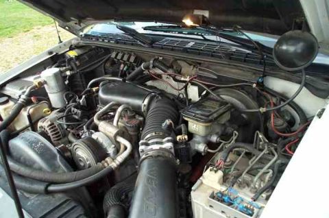1988 Ford Bronco - The engine bay of a vehicle is shown with various mechanical parts and wiring harnesses.