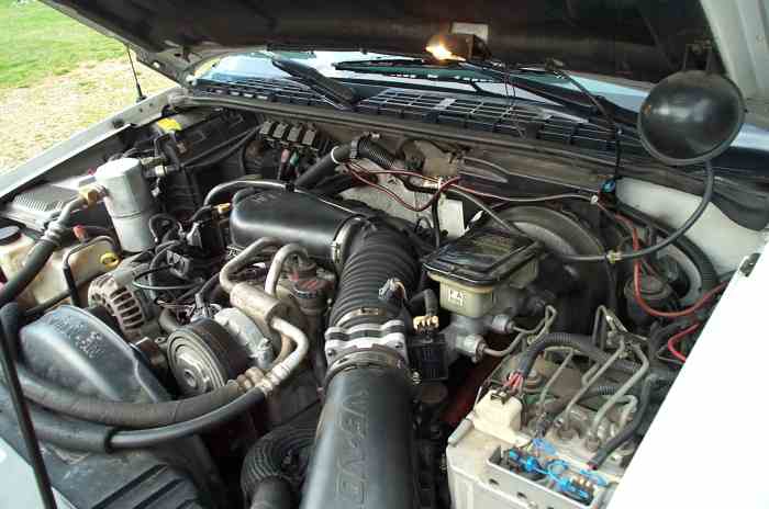 Engine bay with hoses, wires, and engine components visible. Some text on a black air intake tube