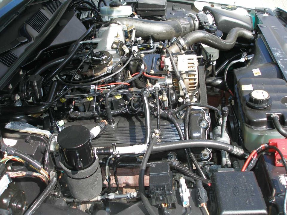 Overhead view of a Ford modular V8 engine bay with black intake manifold and alternator