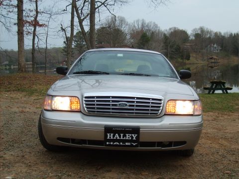 2004 Ford Crown Victoria - A silver 2004 Ford Crown Victoria is shown from the front, parked near a body of water with trees in the background.