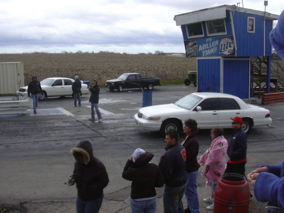 White sedan and black pickup at drag strip. People watching