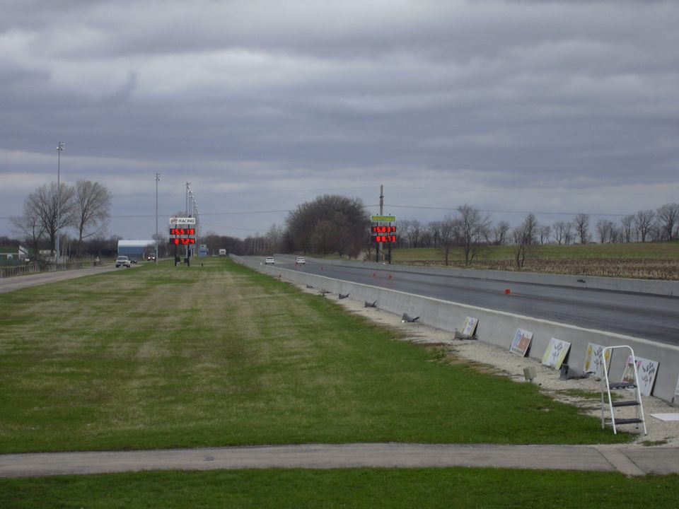 Drag strip with two cars in distance, scoreboard, and SuperMotors logo