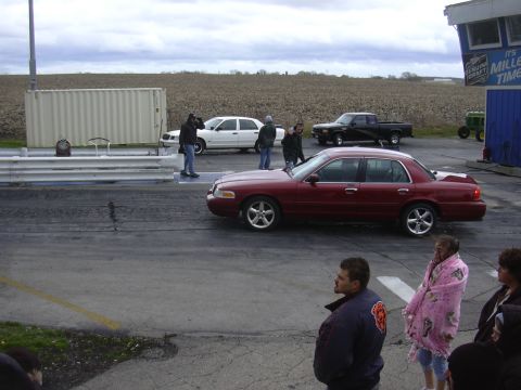 1996 Ford Crown Victoria - Two sedans are lined up on a drag strip, with spectators and a pickup truck nearby.