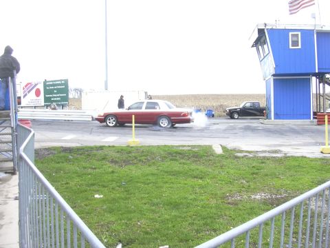 1996 Ford Crown Victoria - A 1996 Ford Crown Victoria performs a burnout on a race track, with a pickup truck in the background.