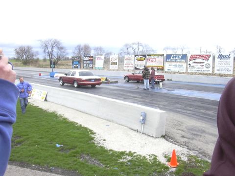1996 Ford Crown Victoria - Cars line up on the drag strip with spectators and advertising billboards visible.