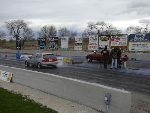 1996 Ford Crown Victoria - A red sedan is parked at a drag strip, with several people gathered around it.