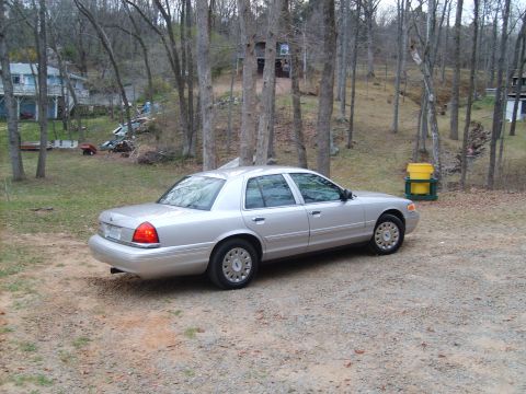2004 Ford Crown Victoria - A silver 2004 Ford Crown Victoria is parked in a wooded area with houses in the background.
