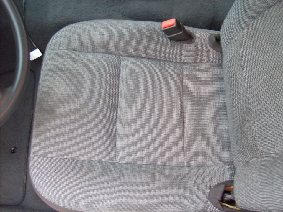 Gray fabric car seat with a visible seatbelt buckle and a dark steering wheel on the left