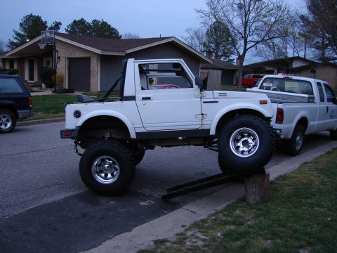 1990 Suzuki Samurai - A modified Suzuki Samurai is positioned on a ramp and a log, with a pickup truck parked nearby.