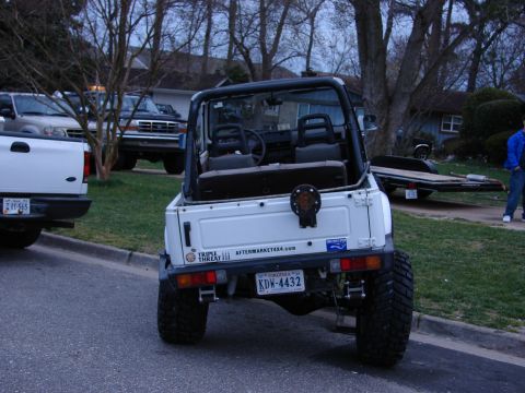 1990 Suzuki Samurai - A white Suzuki Samurai is parked on a street next to other vehicles, with a trailer in the background.