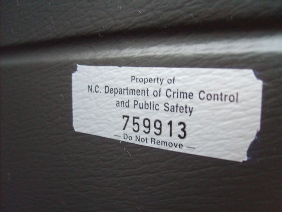 Sticker reading 'Property of N.C. Department of Crime Control and Public Safety 759913 - Do Not Remove' on a dark textured surface