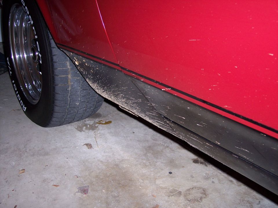 Close-up of a mud-spattered rocker panel on a red car with black pinstripes and a chrome slotted mag wheel