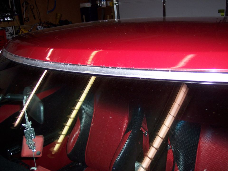 Red car roof and chrome windshield trim, red and black bucket seats visible through glass