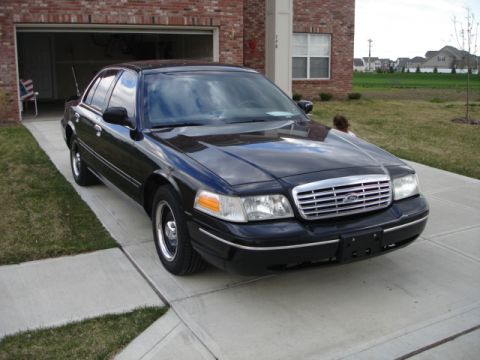 2001 Ford Crown Victoria - A black 2001 Ford Crown Victoria is parked in front of a brick house with an open garage door.