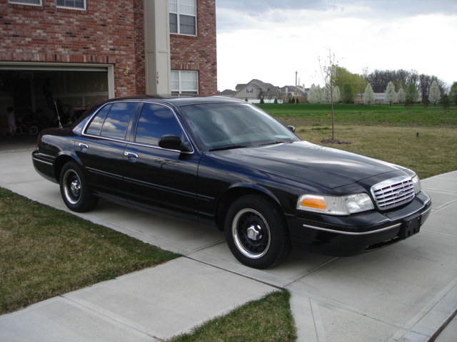 Black 2001 Ford Crown Victoria parked in driveway next to brick building