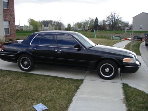 2001 Ford Crown Victoria - A black 2001 Ford Crown Victoria is parked on a driveway in front of a house.