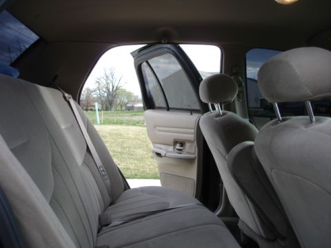 2001 Ford Crown Victoria - The interior of a sedan is shown with the rear passenger door open, revealing the back seat and a view of the outdoors.