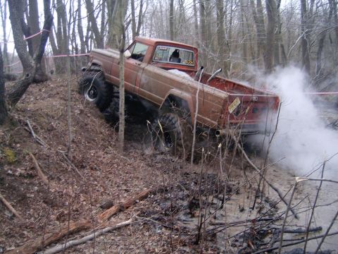 1979 Jeep J-10 - This modified pickup truck is navigating a challenging muddy terrain with significant exhaust smoke.