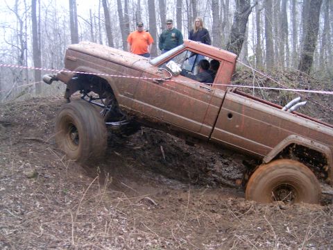 1979 Jeep J-10 - A muddy pickup truck navigates a challenging off-road course with spectators watching.