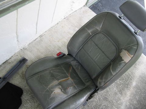 1995 Ford Thunderbird - A worn leather car seat with visible damage is placed on a concrete surface.