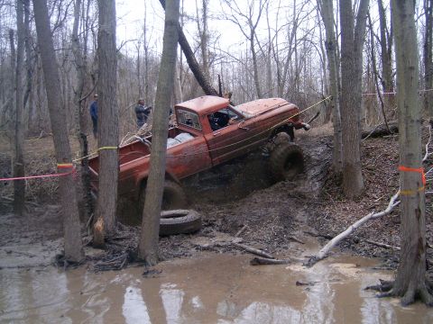 1979 Jeep J-10 - A truck attempts to drive through a muddy, wooded area with two people watching.