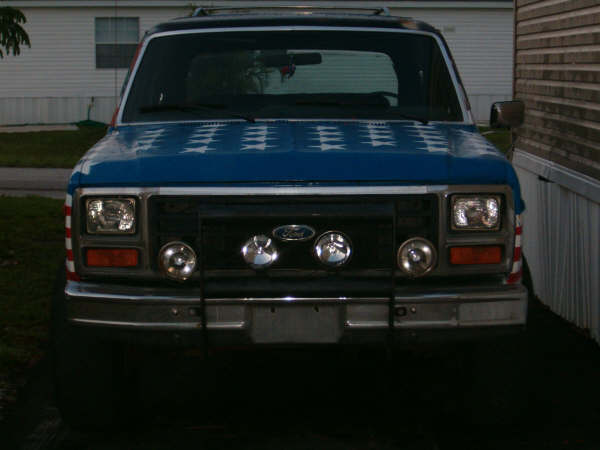 Front view of a blue 1985 Ford Bronco with white stars on the hood and red and white stripes on the fenders