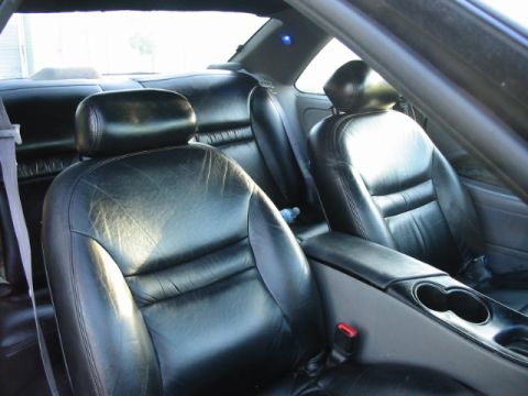 1995 Ford Thunderbird - The interior of a car features black leather seats and a center console with cup holders.