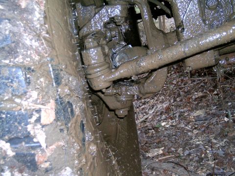 1979 Jeep J-10 - Close-up of a heavily mud-covered vehicle's front suspension and tire, stuck in terrain.