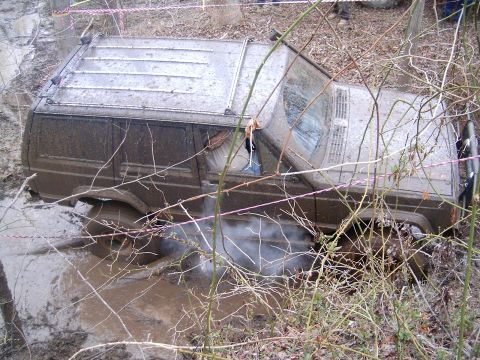 1979 Jeep J-10 - A Jeep Cherokee XJ is stuck deep in mud, with steam or smoke rising from its undercarriage.