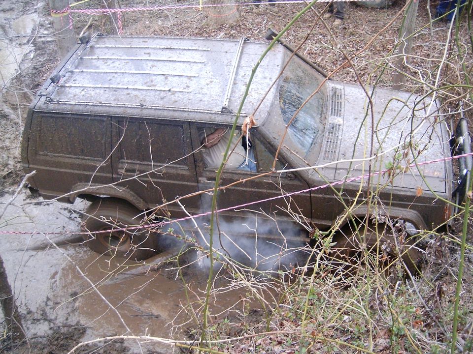 Muddy Jeep Cherokee XJ stuck in a muddy ditch with smoke coming from under the vehicle
