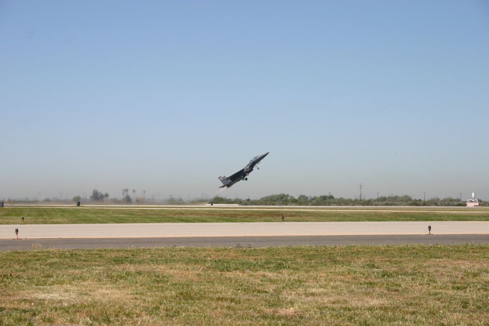 Gray fighter jet climbing after takeoff over a flat airfield runway
