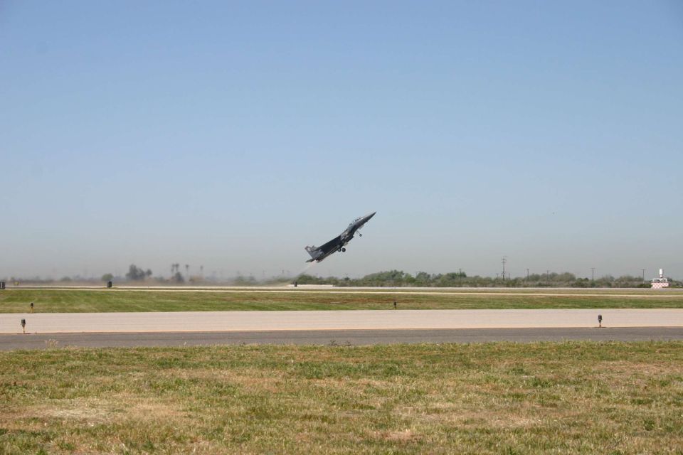 Gray military fighter jet climbing steeply after takeoff from an airfield runway