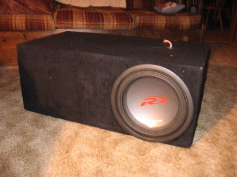1992 Ford Crown Victoria - A black subwoofer with a red Alpine logo sits on a carpeted floor, next to a couch.