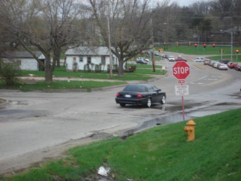 1992 Ford Crown Victoria - A black sedan approaches a stop sign on a cloudy day with other vehicles visible in the distance.