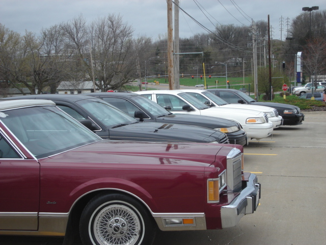 Maroon sedan in foreground, followed by black and white sedans in a parking lot