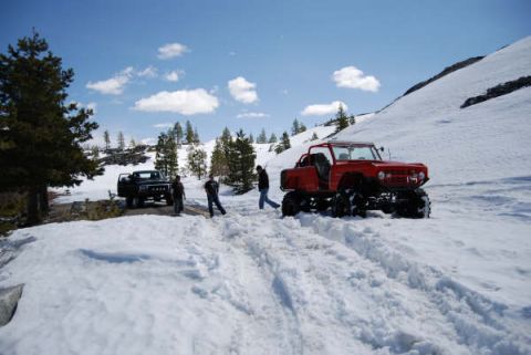 1989 Ford Bronco - Two off-road vehicles are parked in a snowy landscape under a blue sky.