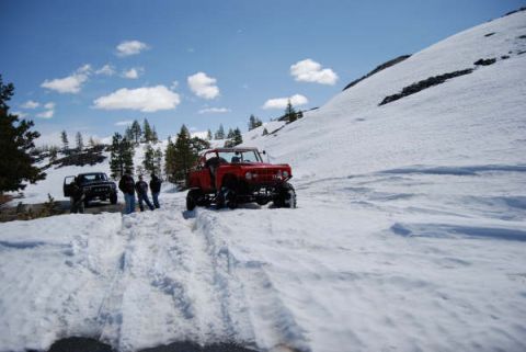 1989 Ford Bronco - Two off-road vehicles are parked in a snowy area with a group of people standing around.