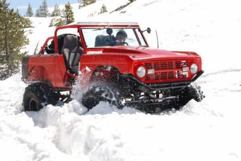 1989 Ford Bronco - This red off-road vehicle navigates a snowy terrain, kicking up snow as it drives.