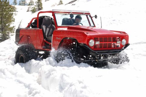 1989 Ford Bronco - First-gen Ford Bronco navigating a snowy landscape, kicking up snow.