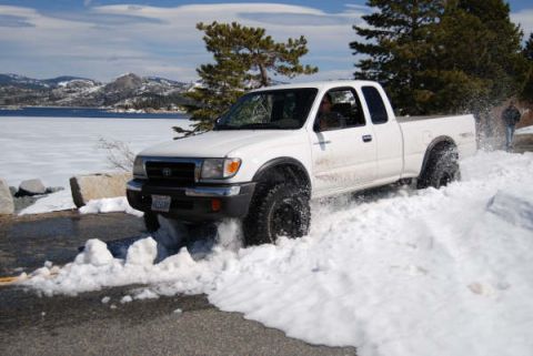 1989 Ford Bronco - A white Toyota Tacoma navigates a snowy road beside a frozen lake.