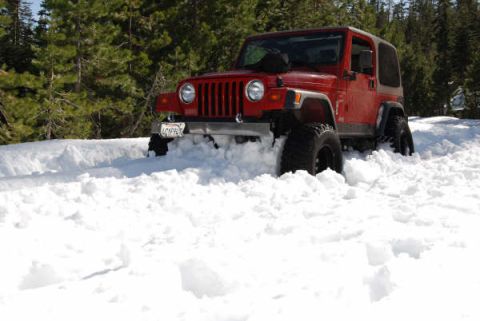 1989 Ford Bronco - A red Jeep Wrangler is partially buried in snow, with trees visible behind it.