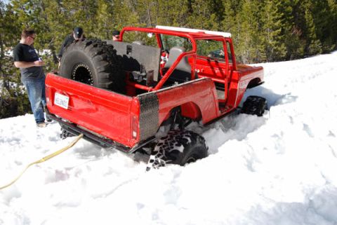 1989 Ford Bronco - A red off-road vehicle with oversized tires is stuck in deep snow, with people standing nearby.