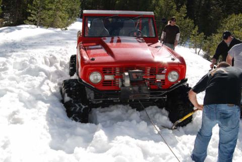 1989 Ford Bronco - A red 1970s Ford Bronco, equipped with a winch, is stuck in deep snow while people attempt to free it.