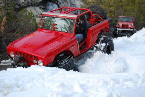 1989 Ford Bronco - A modified red Ford Bronco navigates a snowy trail, with a Jeep Wrangler following in the background.