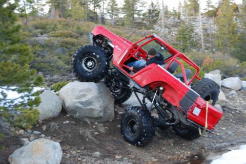 1989 Ford Bronco - Off-road vehicle navigates a rocky incline in a wooded area.