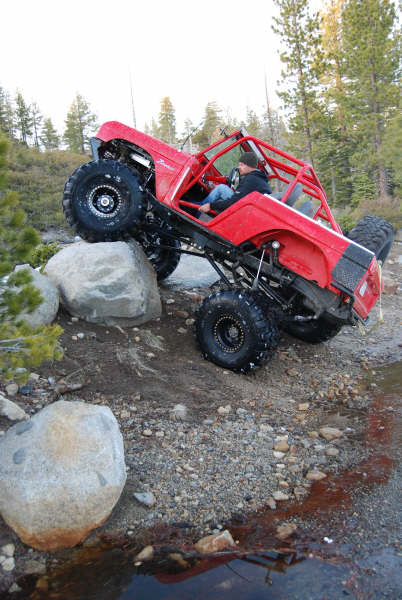 1989 Ford Bronco - This heavily modified off-road vehicle is navigating a rocky trail with a driver behind the wheel.